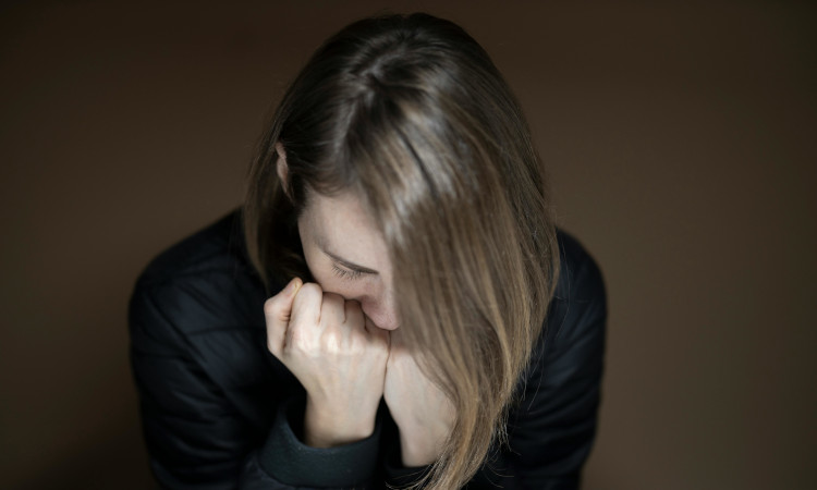 Mulher de camisola preta e cabelo comprido castanho com as m&atilde;os junto &agrave; boca e a cabe&ccedil;a debru&ccedil;ada durante ataque de ansiedade.