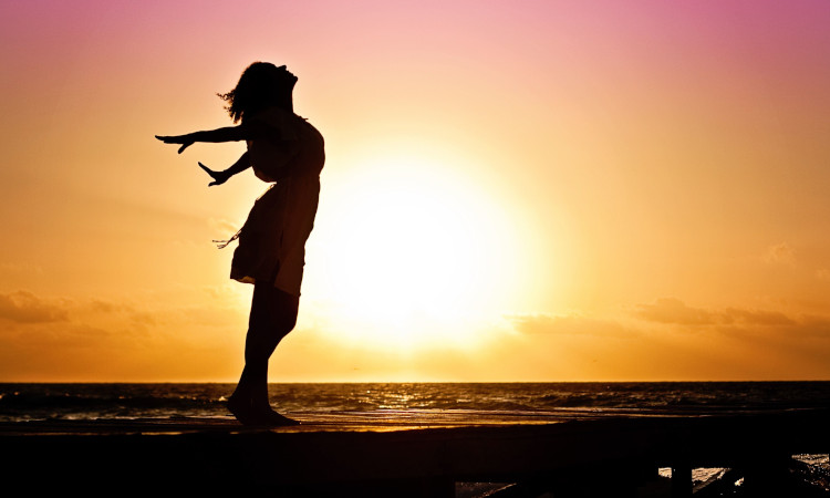 Silhueta de uma mulher na praia com os braços estendidos contra um vibrante pôr-do-sol como pano de fundo, a celebrar a sua liberdade sexual e autodeterminação sexual.