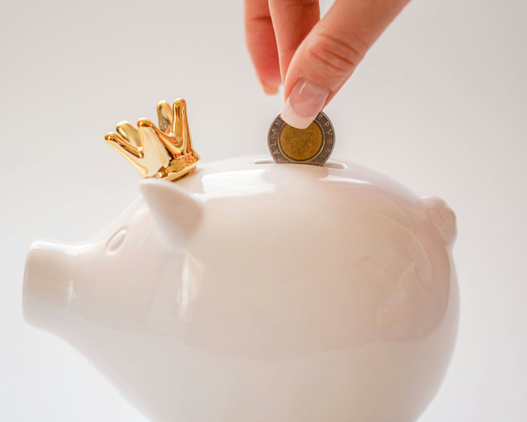 Mão de mulher a colocar moeda em porquinho mealheiro branco e a planear como poupar dinheiro.