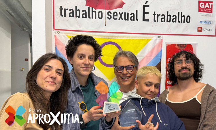 Equipa de cinco técnicos do GAT, incluindo Júlio Esteves de óculos, a sorrir e a segurar Prémio AproXima-te com cartaz em cima a dizer "Trabalho Sexual é trabalho".