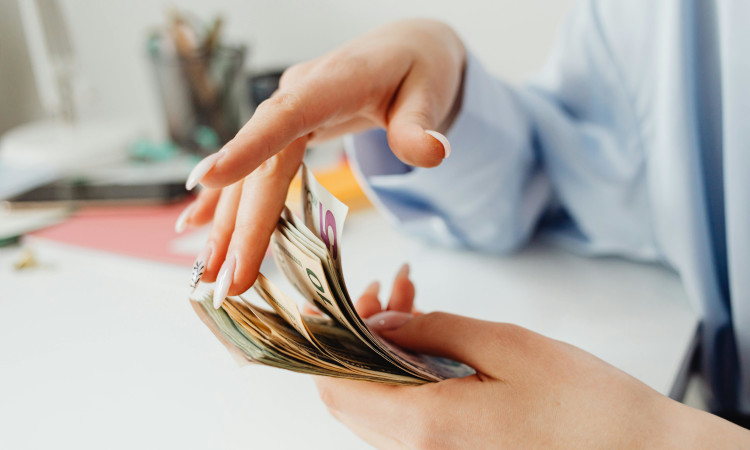 Mãos de mulher a folhear maço de notas e a pensar em como fazer gestão financeira pessoal.