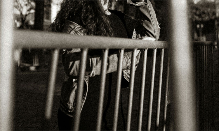 Imagem a preto e branco com corpo de mulher atr&aacute;s de grades, na rua, sem se ver o rosto, enquanto pensa no crime de lenocinio.