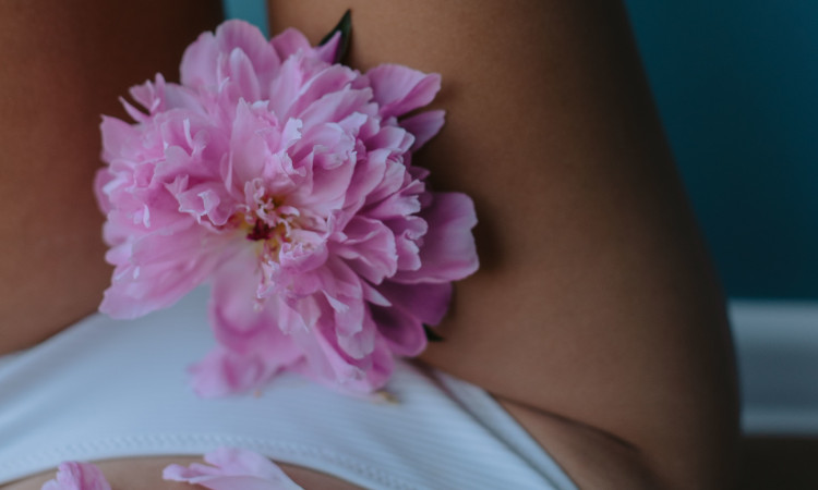 Mulher de cuecas brancas com flor rosa na zona íntima a representar a menopausa.
