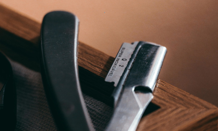 Lâmina de barbear com cabo preto em cima de móvel castanho a representar a mutilação genital feminina.