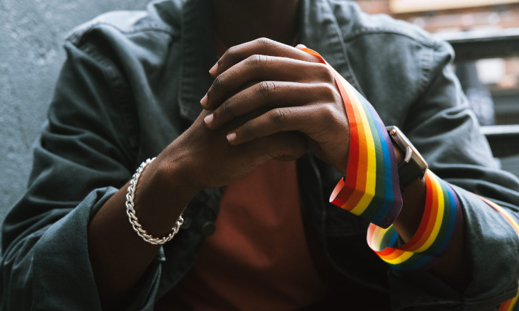 Close-up de mãos entrelaçadas com fita arco-íris a representar o orgulho LGBTQIAPN+ e o outing.