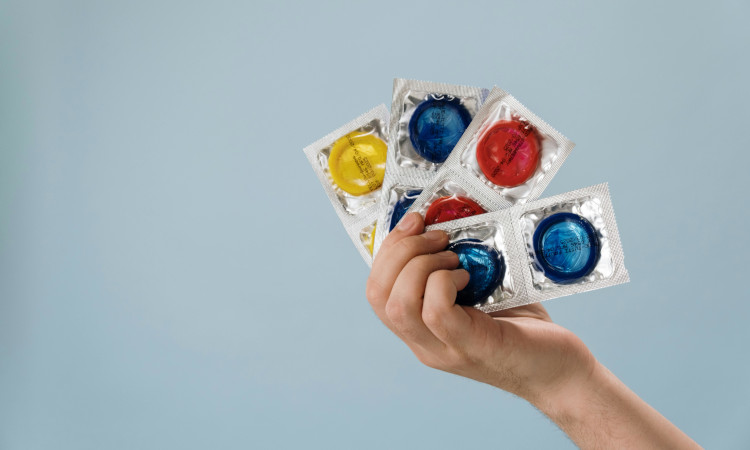 M&atilde;o de mulher a segurar v&aacute;rias camisinhas coloridas e a pensar em como saber o tamanho do preservativo ideal.