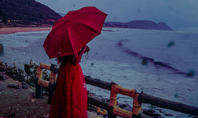 pessoa com vestido e guarda-chuva vermelhos olha para o mar