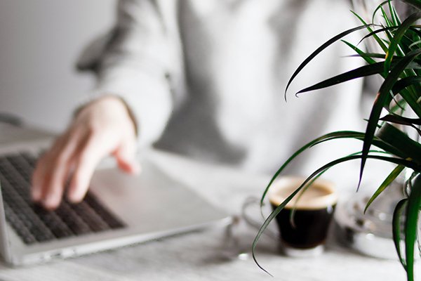 Pessoa a trabalhar no computador com um caf&eacute; e uma planta ao lado representando a parte de emprego
