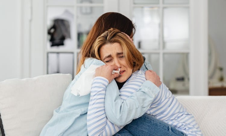 jovem chora abraçada a uma pessoa amiga