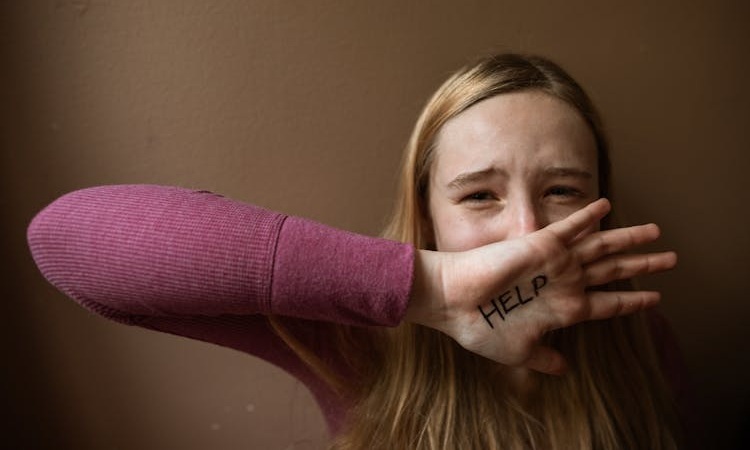 jovem tapa a boca com a m&atilde;o, na qual tem escrito ajuda