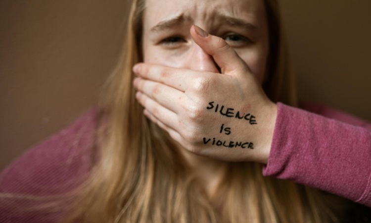 jovem v&iacute;tima de viol&ecirc;ncia no namoro tapa a boca com a m&atilde;o na qual tem escrita a mensagem sil&ecirc;ncio &eacute; viol&ecirc;ncia