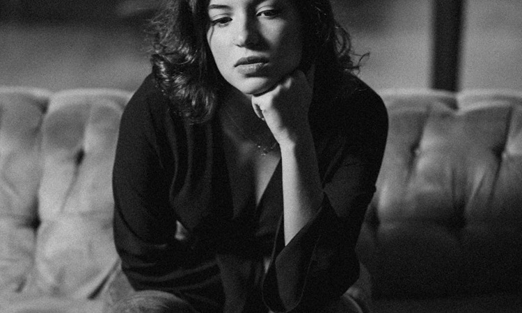 mulher pensativa, sentada no sof&aacute;, com os cotovelos apoiados no joelho e as m&atilde;os a segurar abaixo do queixo