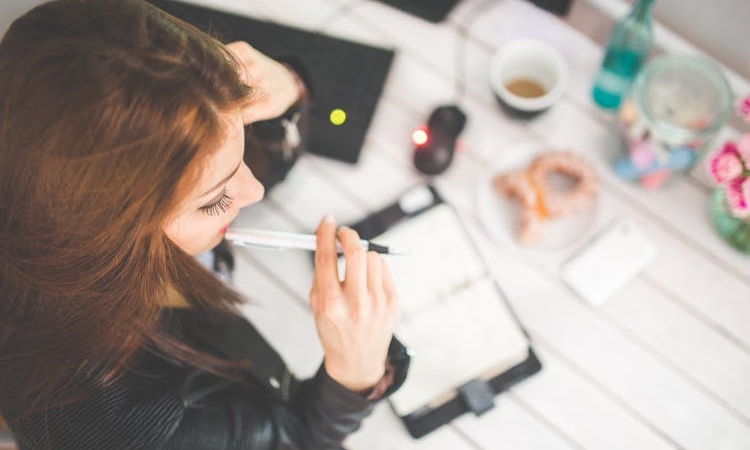 mulher sentada à secretária, pensativa, com caneta na boca