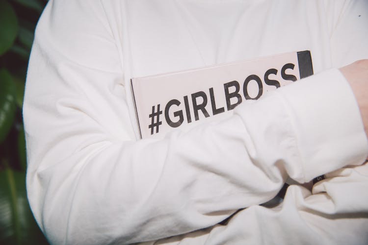 pessoa com camisola branca a segurar um papel onde está escrito girl boss
