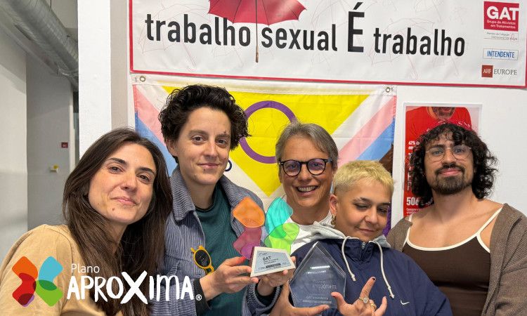 Equipa de cinco técnicos do GAT, incluindo Júlio Esteves de óculos, a sorrir e a segurar Prémio AproXima-te com cartaz em cima a dizer "Trabalho Sexual é trabalho".