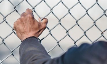 Mão de homem vítima de tráfico de pessoas a agarrar rede.