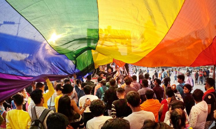 Multidão de pessoas na rua, demonstrando as várias identidades da interseccionalidade com a bandeira LGBPTQI+ desfraldada, preenchendo toda a parte de cima da imagem.