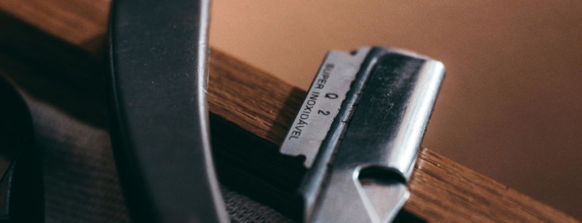 Lâmina de barbear com cabo preto em cima de móvel castanho a representar a mutilação genital feminina.