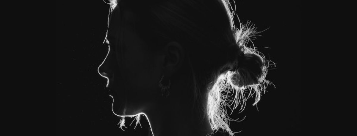 Mulher jovem de perfil, com o cabelo apanhado, num fundo negro - não se vê o seu rosto e representa uma trabalhadora do sexo.