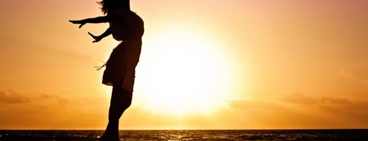 Silhueta de uma mulher na praia com os braços estendidos contra um vibrante pôr-do-sol como pano de fundo, a celebrar a sua liberdade sexual e autodeterminação sexual.