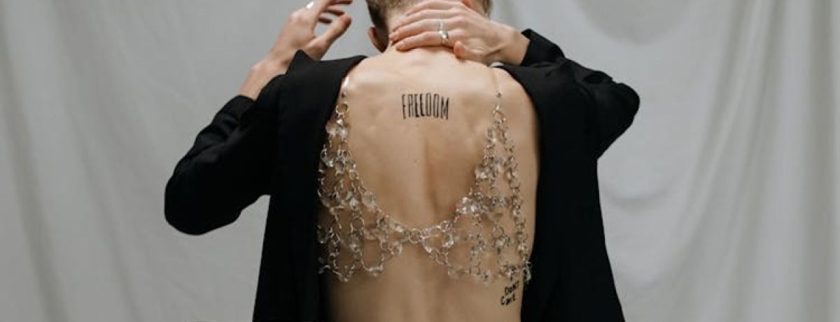 pessoa de costas, mão no pescoço, com tatuagem a dizer freedom nas costas