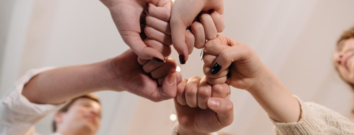 Várias mãos humanas encostadas, com punhos fechados, a representar uma rede de apoio informal.