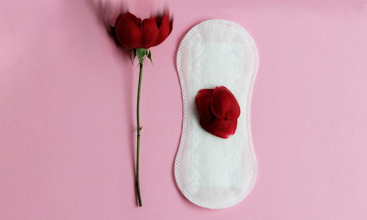 Penso higiénico com pétala vermelha em cima ao lado de uma rosa vermelha a ilustrar o método do calendário.