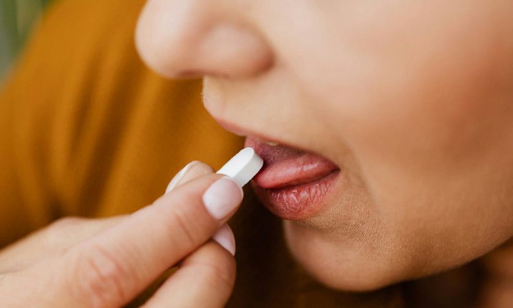 Mão de mulher a levar pílula do dia seguinte à boca, sem se verem os seus olhos.