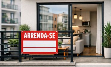 Varanda de apartamento com visão da sala e uma planta no canto, e um letreiro de "Arrenda-se" pendurado.