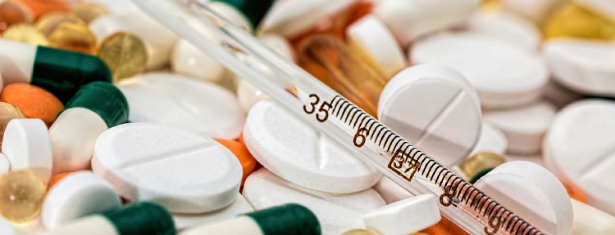 Vários comprimidos de diferentes cores sobrepostos com um termómetro em cima, com medicamos que cortam o efeito da pílula.
