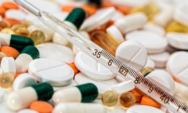 Vários comprimidos de diferentes cores sobrepostos com um termómetro em cima, com medicamos que cortam o efeito da pílula.