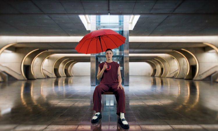 Campanha Invisíveis, mulher sentada numa cadeira, com um guarda-chuva vermelho na mão