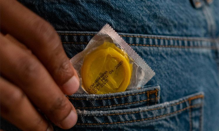 Mão morena a pegar num preservativo do bolso de calças jeans azuis a pensar na sua saúde sexual e reprodutiva.
