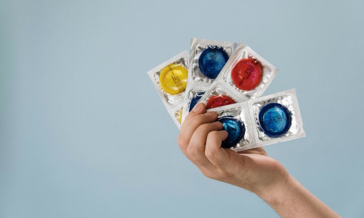 Mão de mulher a segurar várias camisinhas coloridas e a pensar em como saber o tamanho do preservativo ideal.