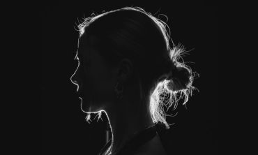 Mulher jovem de perfil, com o cabelo apanhado, num fundo negro - não se vê o seu rosto e representa uma trabalhadora do sexo.