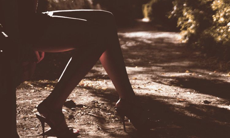 Mulher sentada num banco de jardim, só se vendo as suas pernas em mini saia e salto alto, a fazer trabalho de rua.