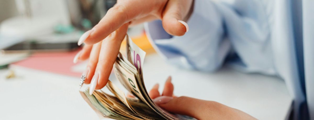 Mãos de mulher a folhear maço de notas e a pensar em como fazer gestão financeira pessoal.