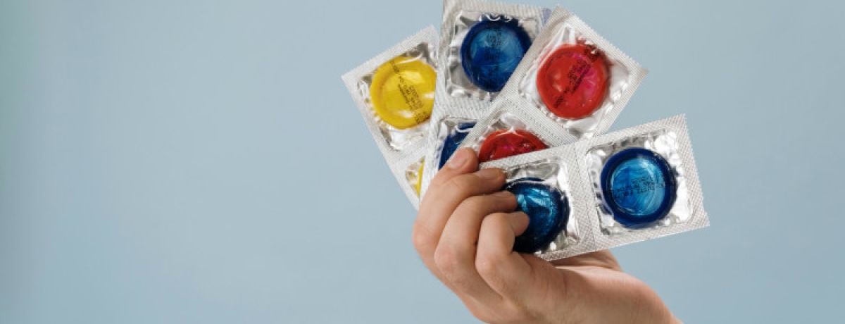 Mão de mulher a segurar várias camisinhas coloridas e a pensar em como saber o tamanho do preservativo ideal.