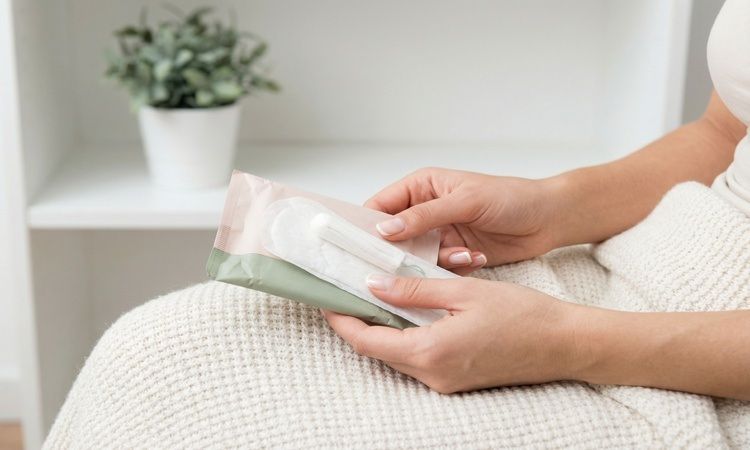 mulher sentada em cama segura em penso higiénico