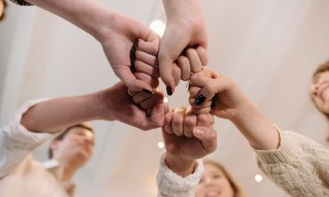 Várias mãos humanas encostadas, com punhos fechados, a representar uma rede de apoio informal.