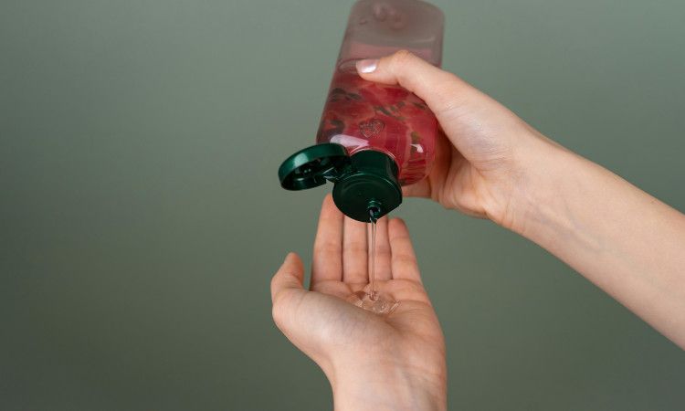 Mão de mulher a segurar lubrificante analgésico em tons rosa e a colocar o gel na outra mão.