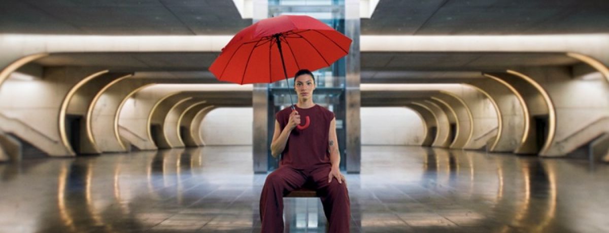Campanha Invisíveis, mulher sentada numa cadeira, com um guarda-chuva vermelho na mão