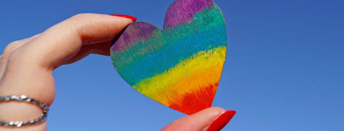 pessoa segura um coração com as cores da bandeira LGBTQIAPN+