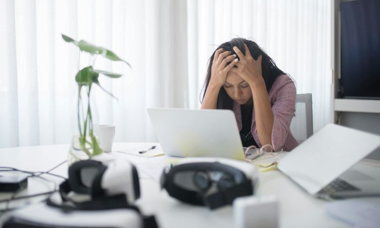 Mulher sentada à secretária com as mãos na cabeça em exaustão devido a burnout.