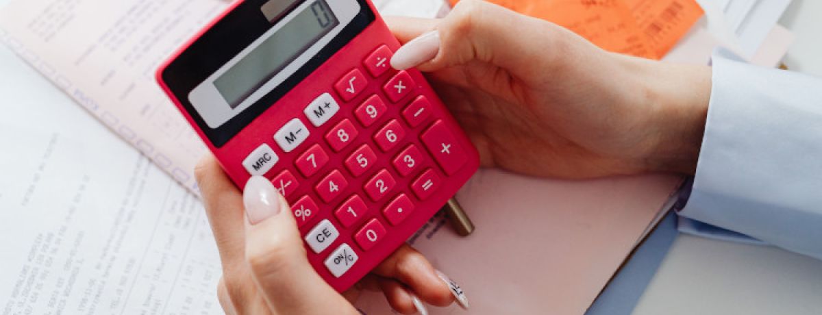 Mãos de mulher a mexer em calculadora vermelha a calcular o ponto de equilíbrio operacional.