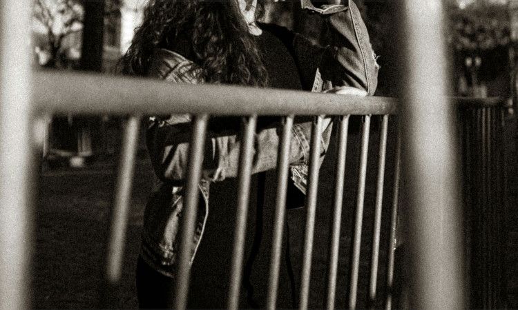 Imagem a preto e branco com corpo de mulher atrás de grades, na rua, sem se ver o rosto, enquanto pensa no crime de lenocinio.