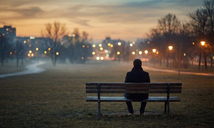 pessoa sozinha, sentada num banco de jardim ao anoitecer
