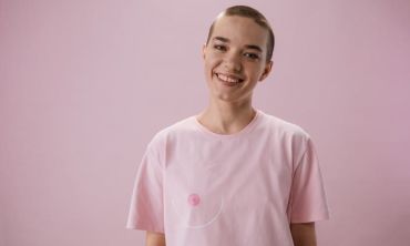mulher transgénero sorri, vestindo uma camisola rosa