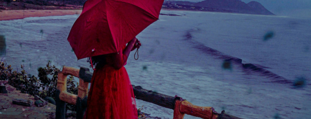 pessoa com vestido e guarda-chuva vermelhos olha para o mar