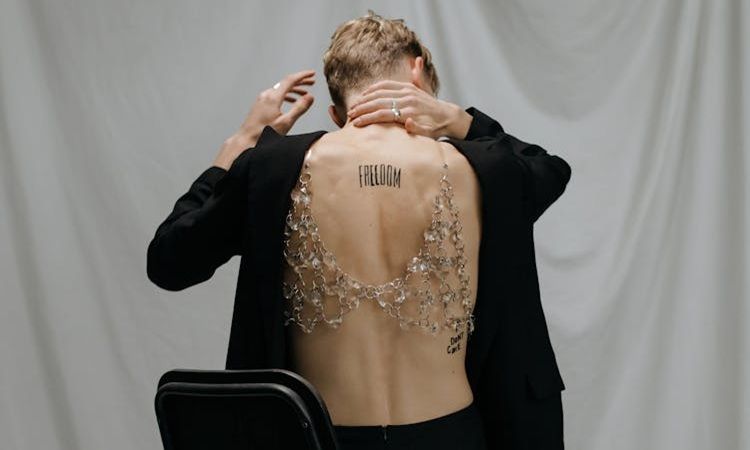 pessoa de costas, mão no pescoço, com tatuagem a dizer freedom nas costas